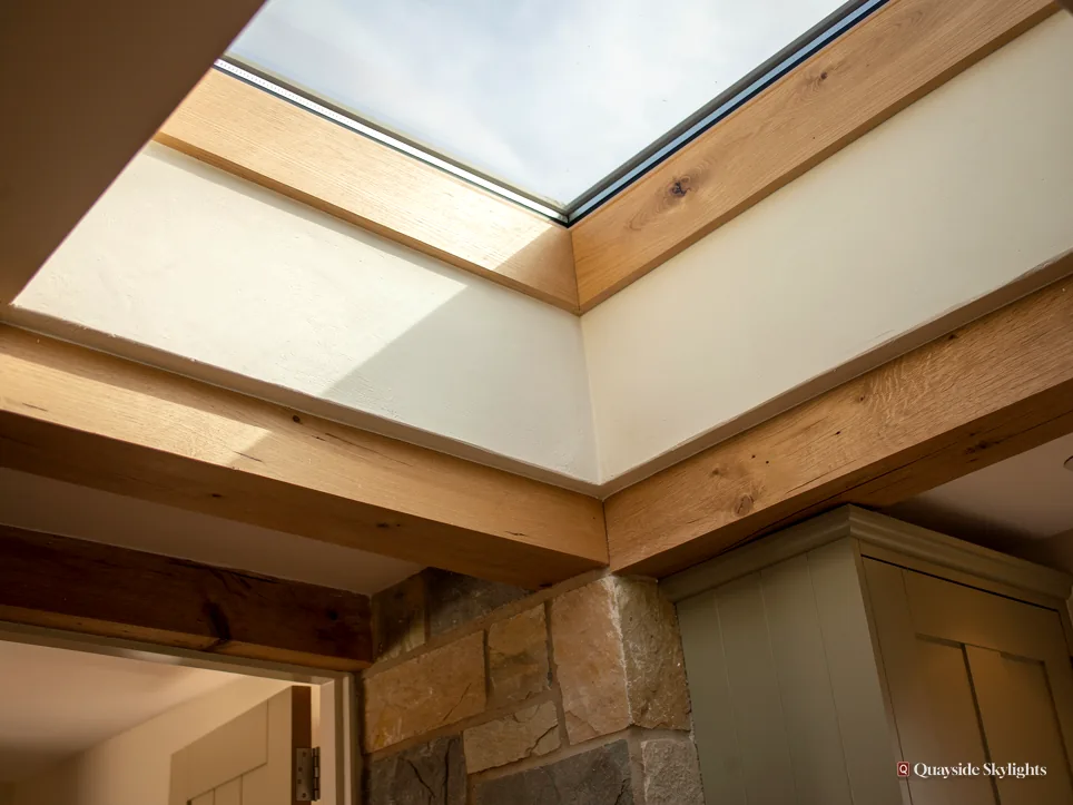 Glass rooflight above an oak beam and exposed stone wall, viewed from beneath